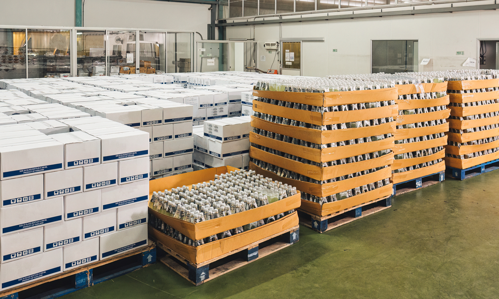 Multiple white boxes and bottles packed and wrapped in bulk piled inside a large warehouse room with bright lights.