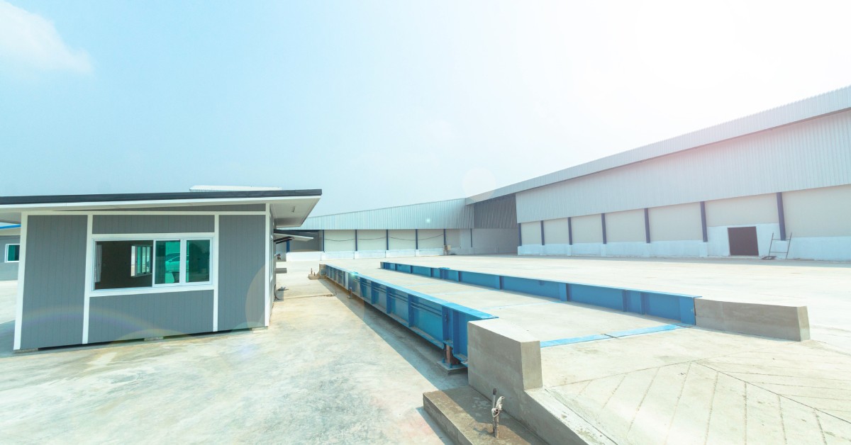 A large blue truck axle scale with a concrete loading ramp next to a small shelter in an industrial environment.