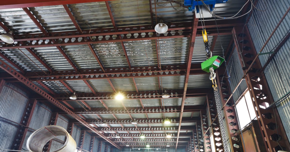 Green scale hanging from a moving hoist placed on a beam on the ceiling inside a large industrial warehouse.