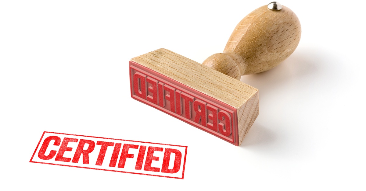 A wood rubber stamper with red ink lies on a white background. The word “Certified” is in red.
