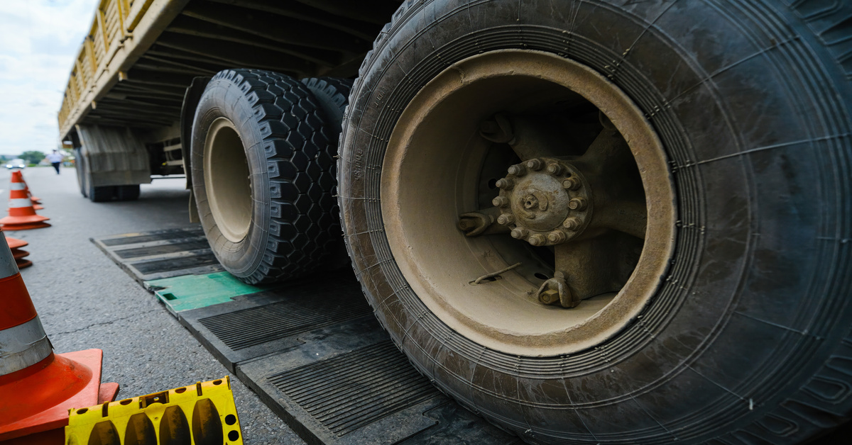 A close-up view shows the large truck wheels sitting on a black and green scale. Orange cones sit next to the scale.