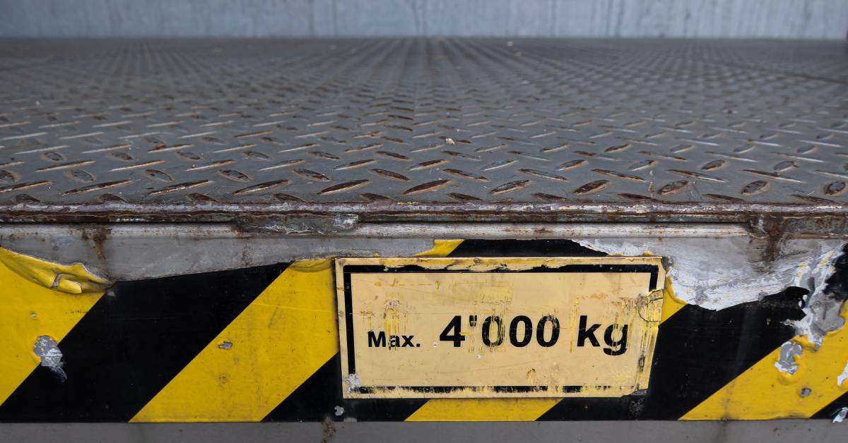 A close-up of the side of an industrial platform scale covered in safety tape that reads "Max. 4'000 kg."