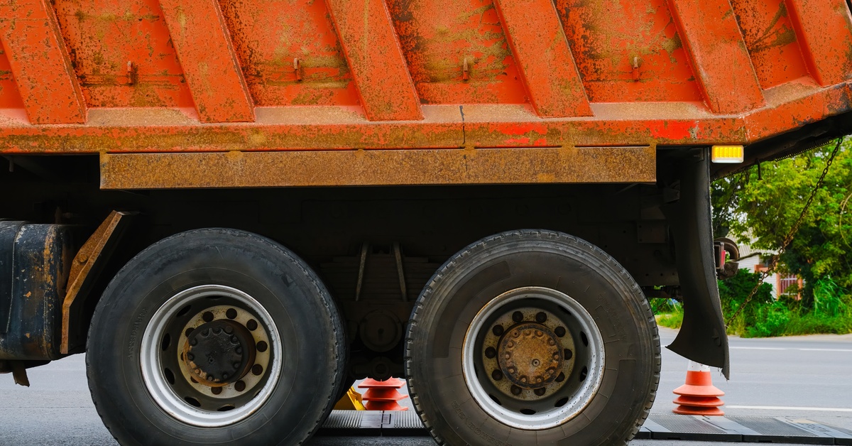 A close-up of a large orange truck parked on top of two electronic axle scale pads. The pads are black and green.